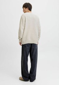 Pull en maille beige clair avec un motif texturé et des poignets côtelés, associé à un pantalon en denim foncé et ample.