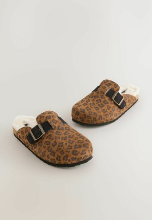 Zoccoli con stampa leopardo marrone, foderati in morbido bianco, con suole nere piatte e doppie cinghie nere con fibbie nella parte superiore.