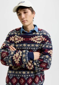 Fleece trui met een patroon in rood, marineblauw, crème en blauw, voorzien van een ronde hals en ribgebreide manchetten. Gelaagd over een spijkerblouse.