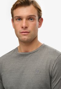 Graues langärmliges T-Shirt mit Rundhalsausschnitt und kleinem gesticktem Logo auf der Brust. Hergestellt aus einem weichen, glatten Stoff.