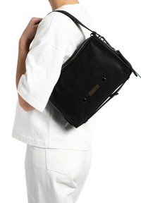 Zwarte leren schoudertas met een rechthoekige vorm, voorzien van een rits, hexagonale hardwareaccenten en een textuurdetail op het oppervlak.