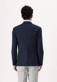 Navy blue blazer with a structured design, single vent, and two buttons, paired with light gray checkered trousers.