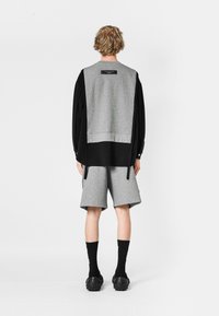Sudadera gris con mangas negras, combinada con pantalones cortos grises. Presenta una etiqueta en la parte posterior y cordones dibujados. Se lleva con calcetines y zapatos negros.