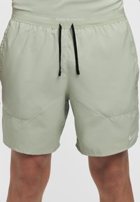 Calções de corrida Nike verdes claros com cós elástico, cordões pretos e bolsos laterais. Apresentam um pequeno logótipo branco na parte inferior da perna.