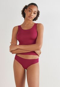 Bordowy bezszwowy top na ramiączkach i pasujące bikini. Materiał jest gładki i elastyczny, z dopasowanym krojem. Minimalistyczny styl z szerokimi ramiączkami.