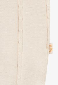 Υφασμα πλεκτό σε κρεμ χρώμα με κάθετο σχέδιο κοτσίδας και μια μπεζ ετικέτα με την επιγραφή «BLEVVE» στη δεξιά άκρη.