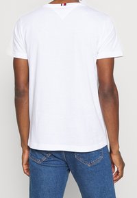 Camiseta blanca de algodón con mangas cortas, con un corte en forma de V en la parte posterior del cuello con rayas en rojo, blanco y azul. Corte clásico.