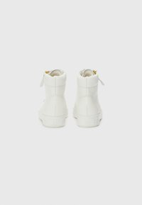 Weiße High-Top-Sneaker mit einer glatten Lederoberfläche, ausgestattet mit einem goldenen Reißverschluss-Akzent und einer strukturierten Gummisohle, von hinten betrachtet.