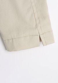 Béžová bavlněná látka s hladkým povrchem, s bočním rozparkem a upraveným švem podél spodního okraje. Design zdůrazňuje jednoduchost a funkčnost.