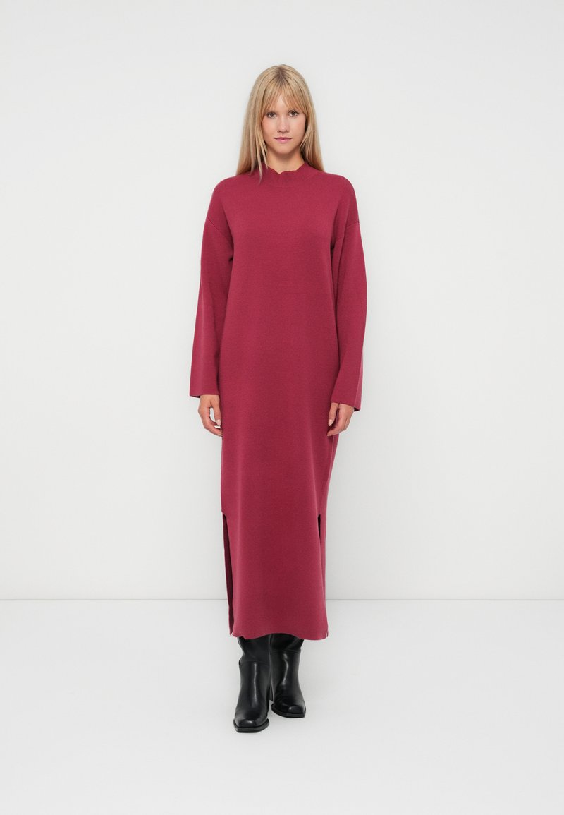 Vestito long-sleeve bordeaux con colletto alto, fessure laterali e vestibilità ampia, abbinato a stivali neri al ginocchio. Tessuto morbido.