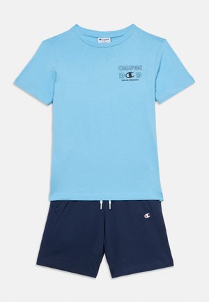 Tricou bleu deschis din bumbac, cu mâneci scurte, având un mic logo negru "Champion". Asortat cu pantaloni scurți bleumarin, talie elastică, cu detaliu logo.