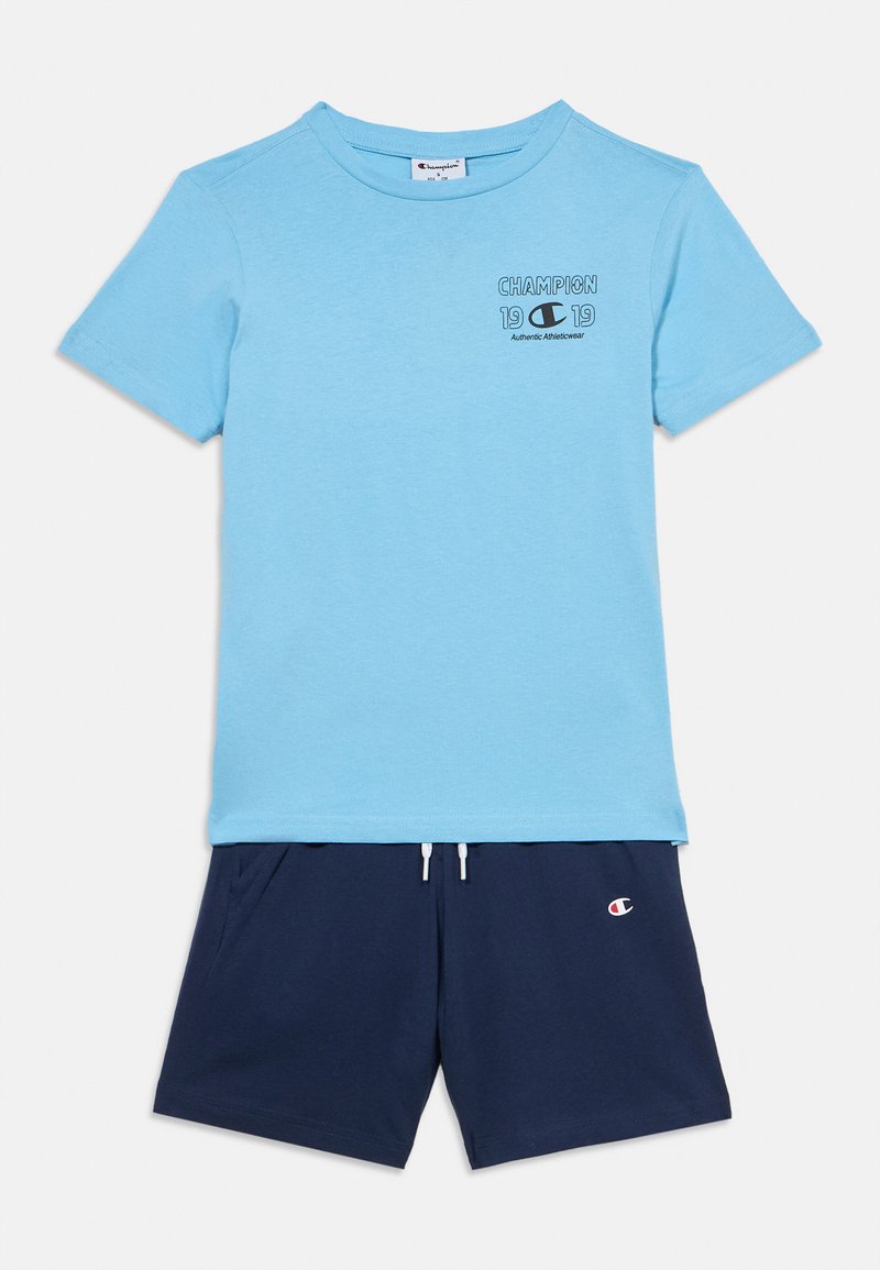 Ανοιχτό μπλε βαμβακερό μπλουζάκι με κοντά μανίκια, με μικρό μαύρο λογότυπο "Champion". Συνδυάζεται με σορτς ναυτικού μπλε χρώματος, με ελαστική μέση και λεπτομέρεια λογοτύπου.