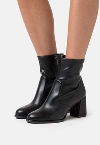 Black leather ankle boots with a smooth texture, square toe, side zipper, and chunky block heel. Elevated design for versatile wear.