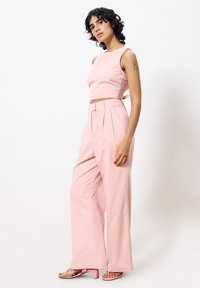 Lichtroze crop top met een strikdetail, gecombineerd met hoge, wijde broekspijpen. Glad materiaal, eenvoudig ontwerp en subtiele plooien.