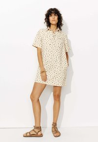 Robe beige à manches courtes avec imprimé floral noir, dotée d'un col et d'une poche avant. Associée à des sandales à lanières marron.