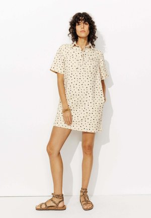 Robe beige à manches courtes avec imprimé floral noir, dotée d'un col et d'une poche avant. Associée à des sandales à lanières marron.