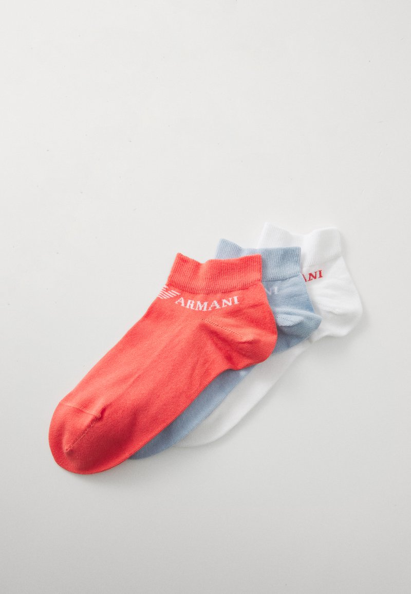 Trois paires de chaussettes courtes : une corail, une bleu clair et une blanche, fabriquées en tissu lisse avec le logo 'Armani' sur les motifs.