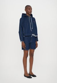 Denimjakke med hætte og frontlomme, med snøre lukning; parret med matchende denimshorts. Mørkeblåt stof med syninger som accent.
