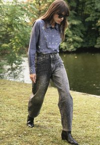 Chemise en denim avec des embellissements floraux, associée à un jean noir déchiré orné de clous en argent. Modèle portant des bottines noires.