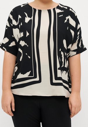 Losse zwart-wit blouse met korte mouwen met abstracte en verticale streeppatronen, gedragen met zwarte broek.