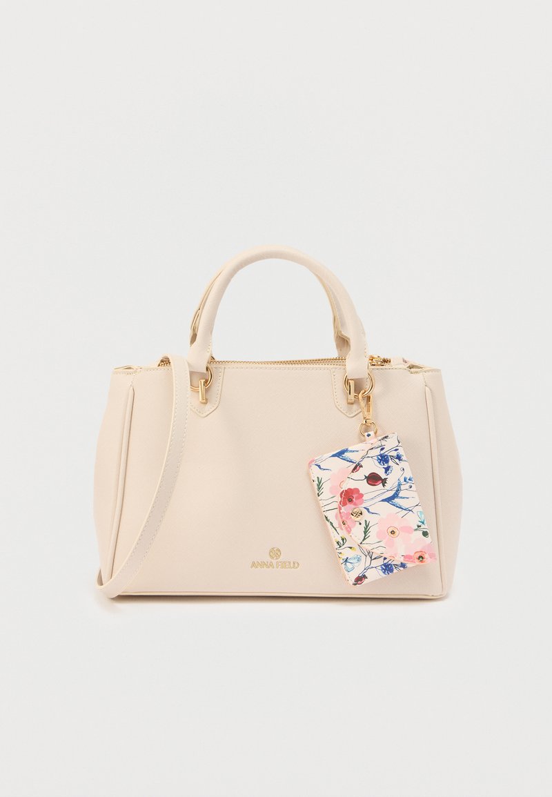 Sac à main beige avec deux poignées et une bandoulière, doté d'un porte-cartes à motif floral attaché par un fermoir doré.