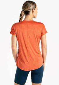 Kurze ärmeliges orangenes Sportoberteil mit strukturiertem Finish, abgerundetem Saum und dezenten Nähten, kombiniert mit marineblauen Shorts.