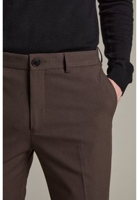 Bruna skräddarsydda byxor med en mjuk textur, bältesöglor och en framficka. Har en enkel knappstängning och en rak passform.