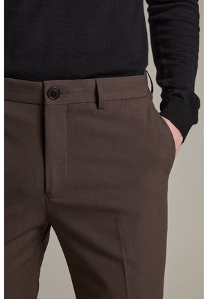 Pantaloni tailleur marroni con una texture liscia, passanti per cintura e una tasca anteriore. Presentano una chiusura a un bottone e un design a gamba dritta.