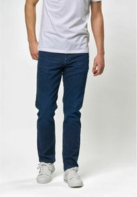 Mörkblå denimjeans, slim fit, med en klassisk femficksdesign. Bärs tillsammans med en enkel vit t-shirt och vita sneakers.