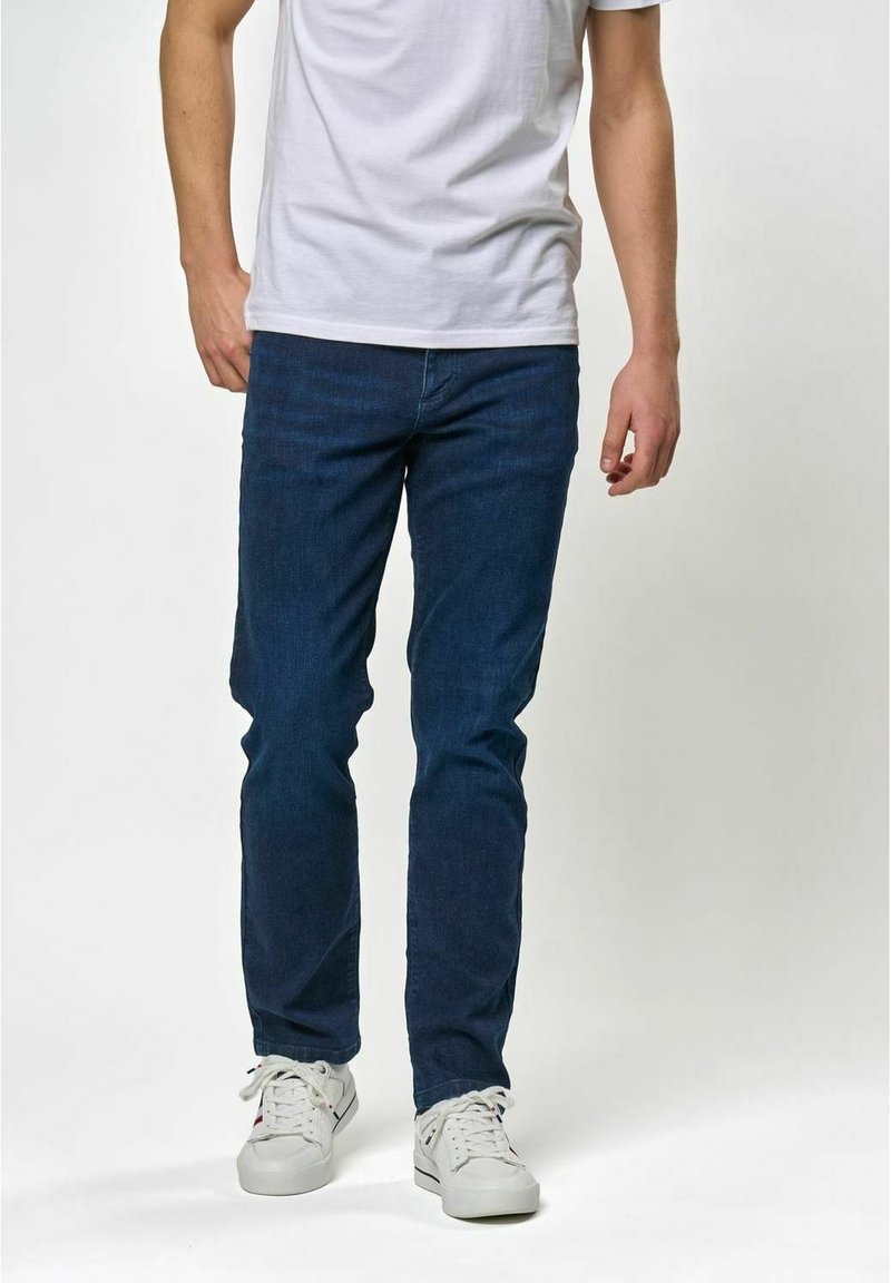 Mörkblå denimjeans, slim fit, med en klassisk femficksdesign. Bärs tillsammans med en enkel vit t-shirt och vita sneakers.