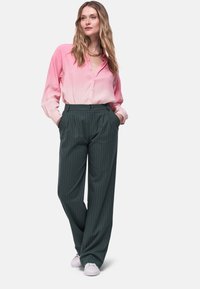 Lichtroze ombre shirt met knopen aan de voorkant, gecombineerd met donkergroene gestreepte broek. Model draagt witte sneakers.