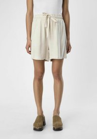 Lyse beige, mellemlange shorts med elastisk talje og bindedetalje. Glat, struktureret stof. Kombineret med brune hælede mule-sko.