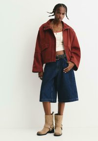 Rode cropped jas met hoge kraag, beige tanktop, losse donkere denim shorts en tan kleurige suède enkellaarsjes met gespen.