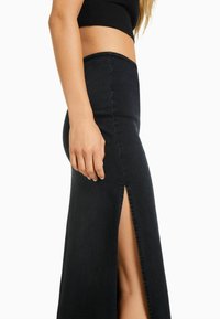 Falda de mezclilla negra con una abertura lateral, cintura ajustada y textura suave. El diseño presenta una silueta elegante que acentúa la pierna.