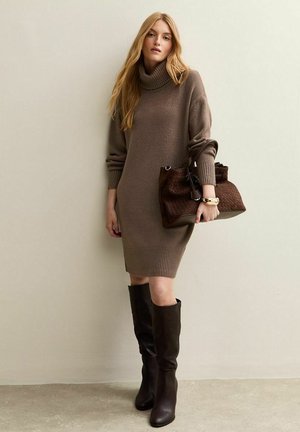 Robe tricotée marron avec col roulé et poignets côtelés, associée à de grandes bottes en cuir marron foncé et à un sac à main texturé marron.
