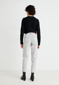 Suéter preto de malha, jeans cinzentos de cintura alta e botins pretos até ao tornozelo. Os jeans têm um corte reto, cinco bolsos e um acabamento desbotado.