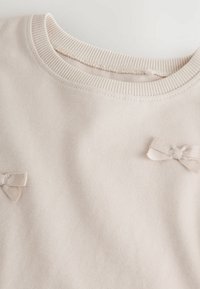 Light pink sweatshirt featuring a ribbed neckline. Two small fabric bows are attached to the front for added detail. Soft texture.