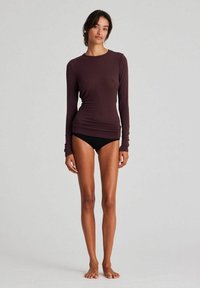 Ilgas rankovės, prigludęs viršus, pagamintas iš švelnaus, tampraus audinio tamsiai rudos spalvos, derinamas su juodais bikini apatiniais. Lygus paviršius, paprastas dizainas.