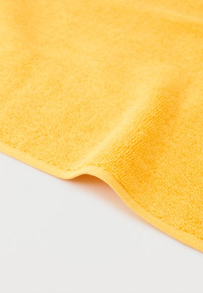 Μαλακό κίτρινο πετσετέ ύφασμα με διπλωμένη άκρη, τοποθετημένο σε λευκή επιφάνεια.