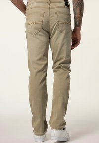 Pantalones de mezclilla beige con corte recto, con costuras en contraste y dos bolsillos traseros. Combinados con zapatillas blancas.