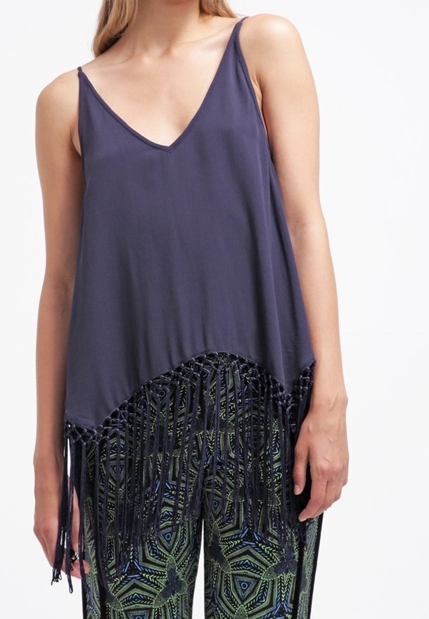 Femme portant un haut sans manches bleu marine avec un ourlet à franges, associé à un pantalon à motifs géométriques verts et bleus.