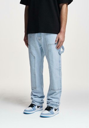 Lichtblauwe denim cargobroek met zijzakken, gestikte details en een relaxed fit, gecombineerd met zwart-witte sneakers.