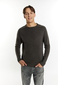 Maglione a maglia grigio scuro con scollo rotondo, polsini e orlo a costine. Indossato sopra jeans grigio chiaro, esposto su uno sfondo bianco.