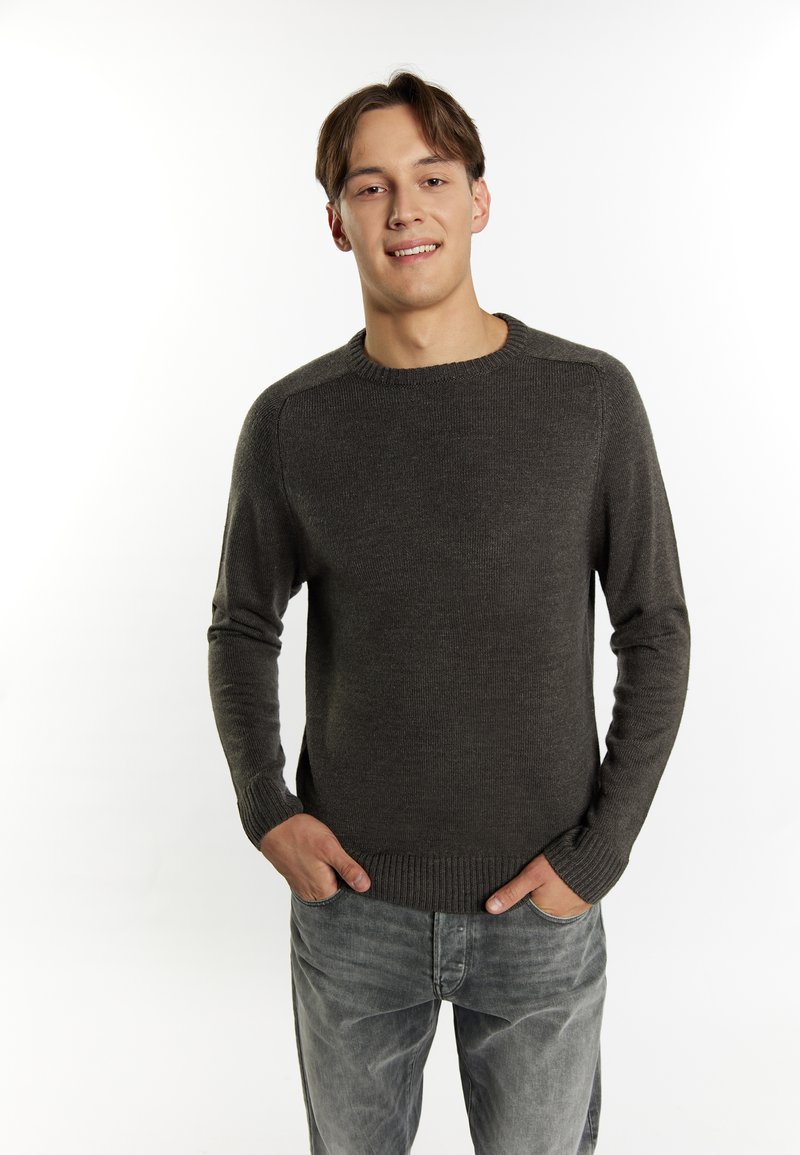 Maglione a maglia grigio scuro con scollo rotondo, polsini e orlo a costine. Indossato sopra jeans grigio chiaro, esposto su uno sfondo bianco.