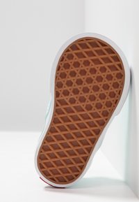 Ruskea kumipohja, jossa on teksturoitu, geometrinen kuvio, ympäröity valkoisella kumireunalla ja vaaleansinisellä yläosasuunnittelulla.