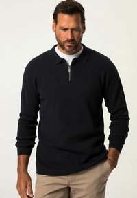 Marinefarbener Pullover mit Viertel-Reißverschluss-Kragen, gerippten Bündchen und weicher Textur, getragen über einem weißen Rundhalsausschnitt-Shirt.