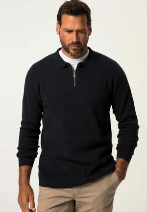 Marinefarbener Pullover mit Viertel-Reißverschluss-Kragen, gerippten Bündchen und weicher Textur, getragen über einem weißen Rundhalsausschnitt-Shirt.