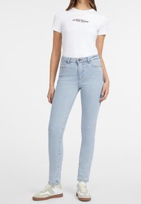 Ljusblå skinny jeans med hög midja, denimmaterial, femfickorsdesign och kontrasterande sömmar, i kombination med en vit t-shirt med logga och sneakers.