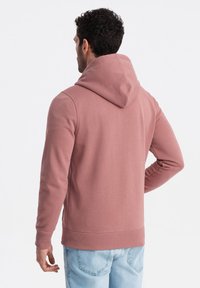 Sweat à capuche rose clair avec des poignets et un ourlet côtelés, texture douce et poche kangourou, porté avec un jean bleu clair.