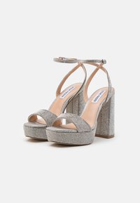 Silberne Plateau-Sandalen mit offener Zehe, ausgestattet mit einem breiten Vorderriemen, einem Knöchelriemen und einem strukturierten Blockabsatz, der mit Strasssteinen verziert ist.